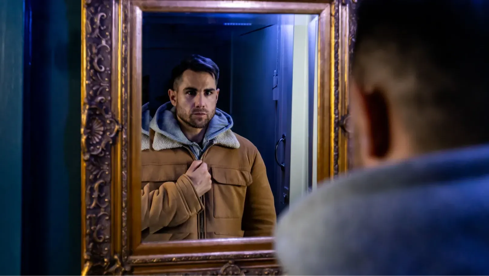 A man stares at his reflection in a hallway mirror.