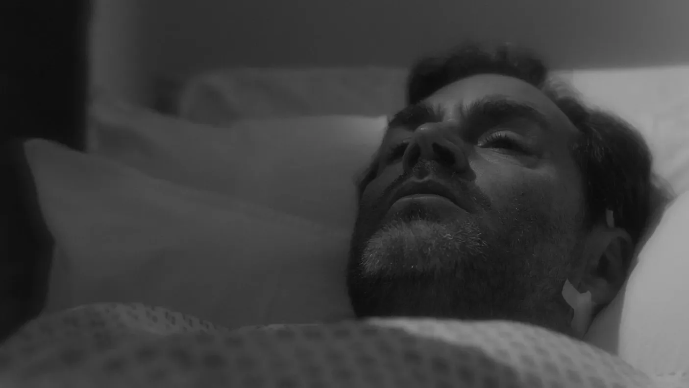 A man lying in bed, post surgery with a bandage on his ear.