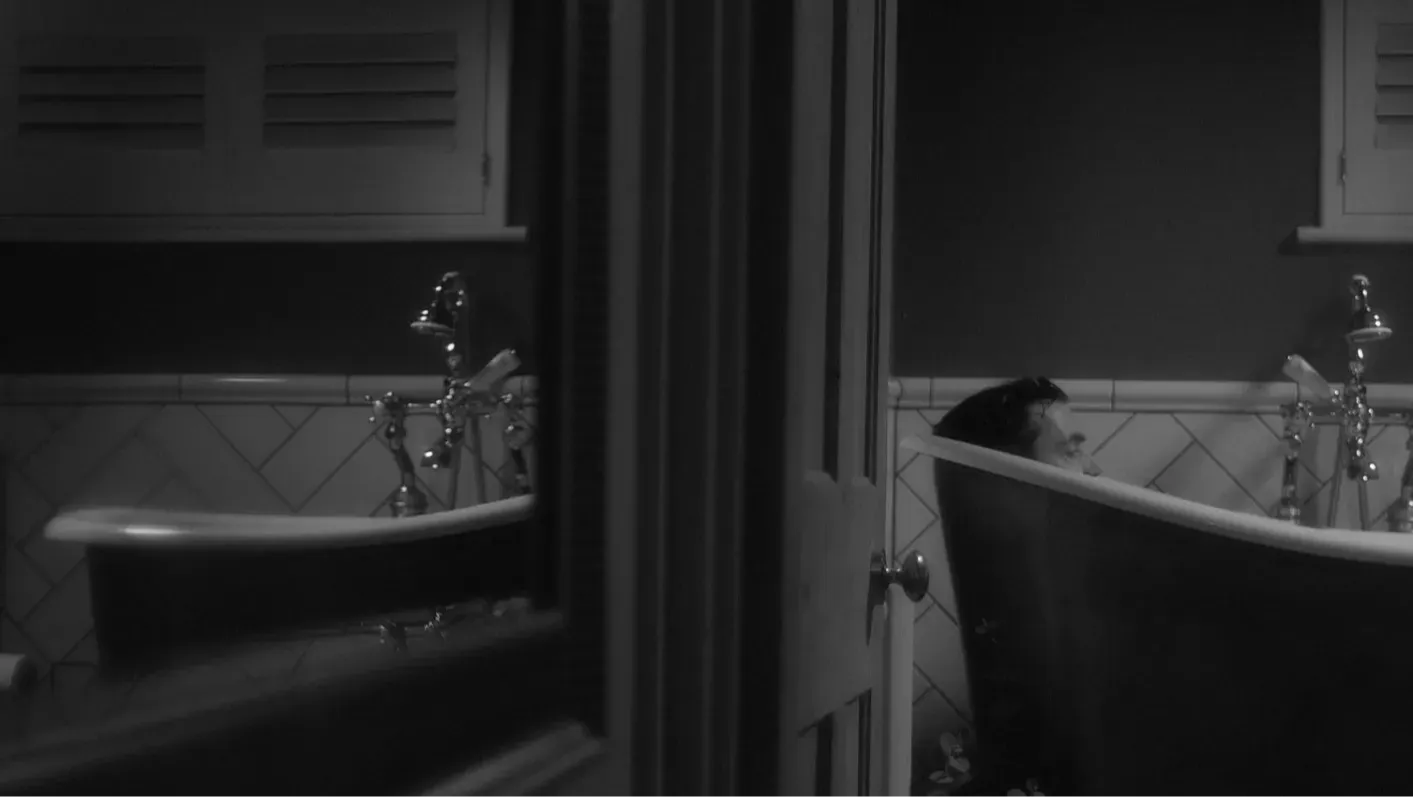 A man sitting in bath tub, with image reflected in mirror.