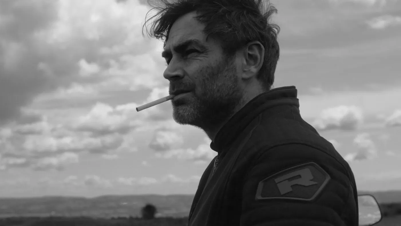 A man smoking a cigarette, standing on top of a hill.