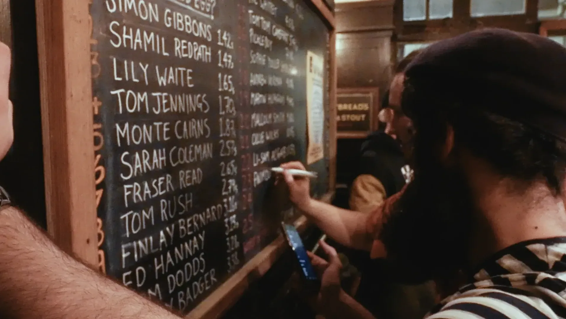 Two men write names and times on a board measuring times of how fast people eat pickled eggs
