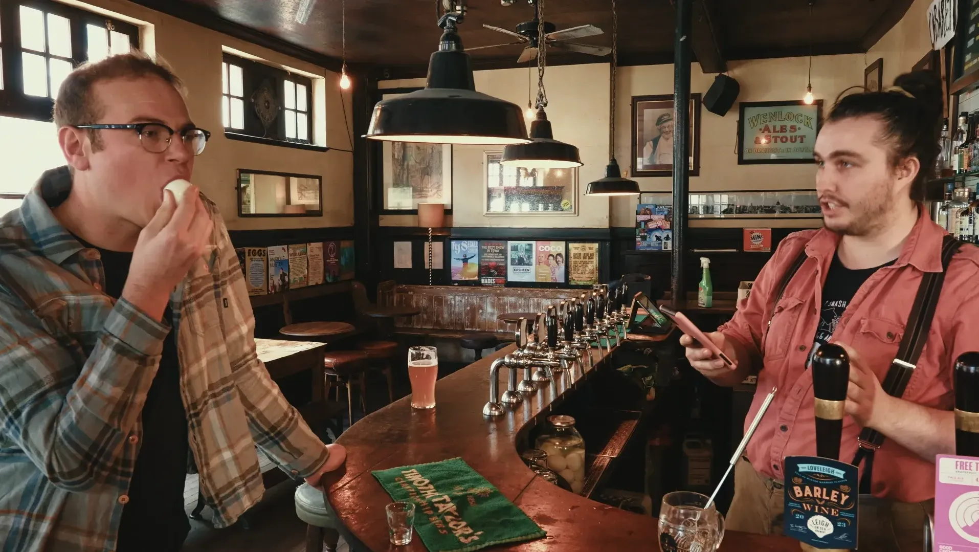 A man is in a pub ready to eat a pickled egg while another man holds a phone ready to time him
