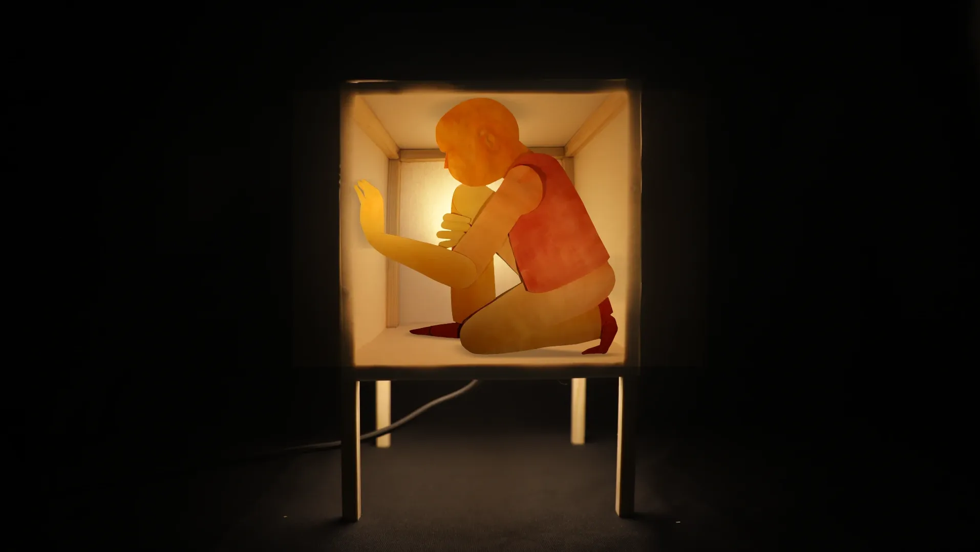 A paper cut-out person kneeling down inside a cubic paper lamp