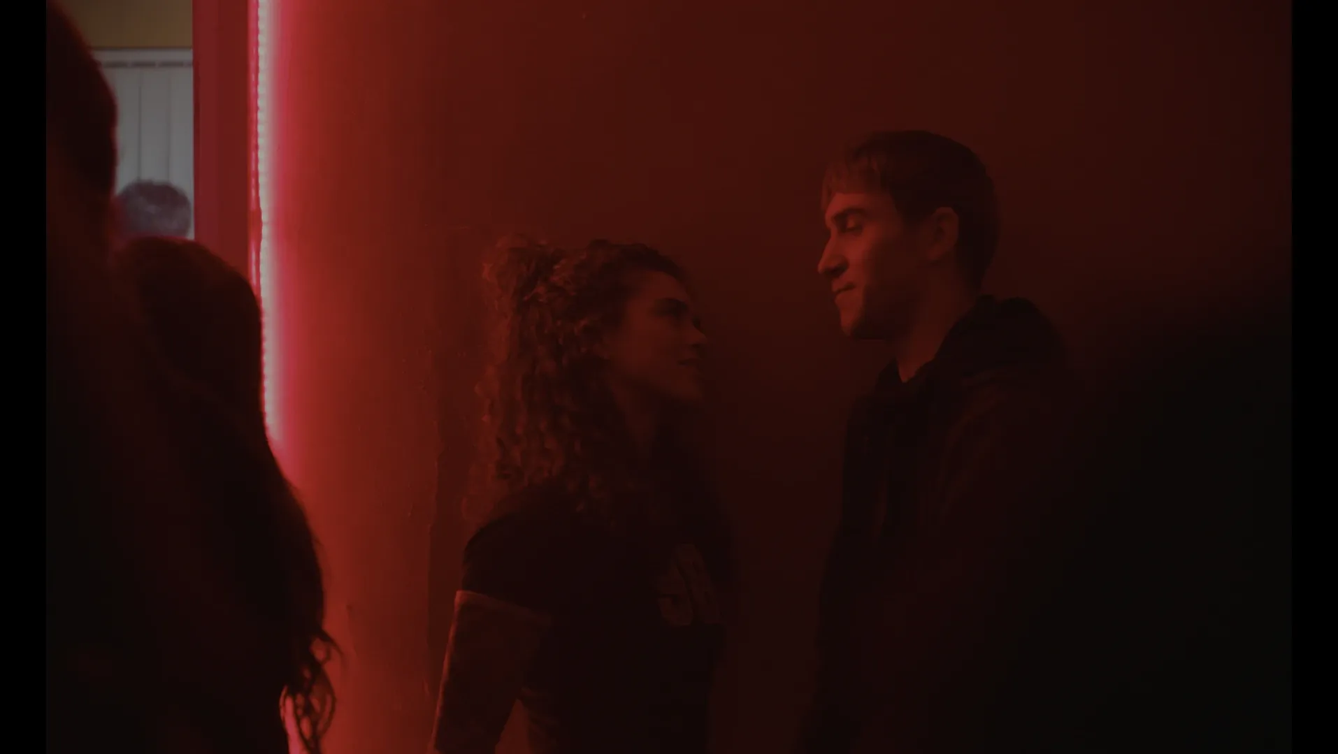 A young woman stands in red hazy room next to a young man