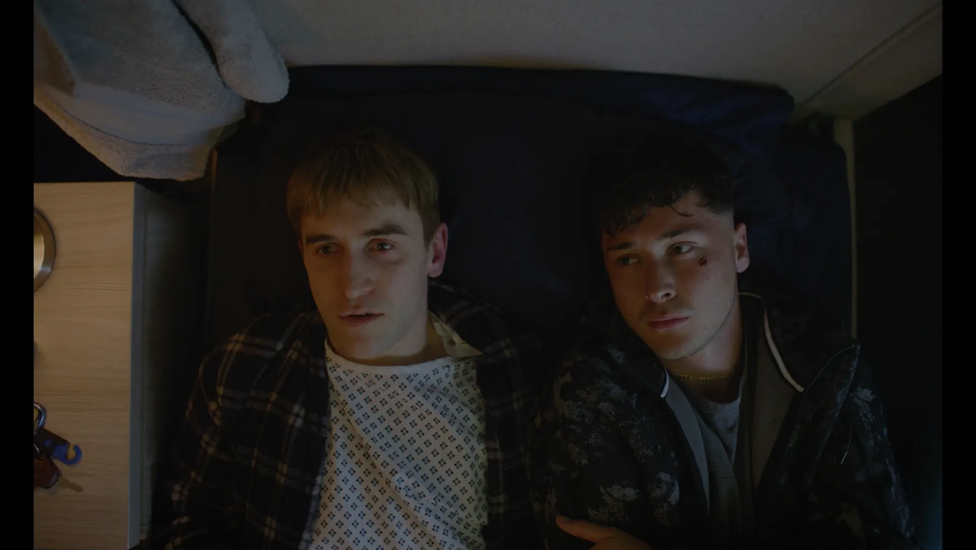 A young man lays next to another, both are deep in thought.