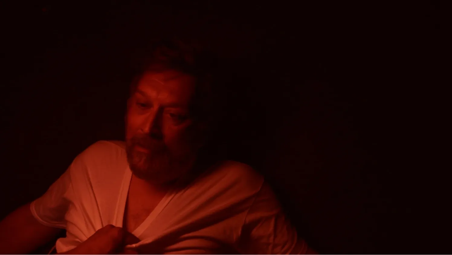 A man in a dark room illuminated by red light that is being held on the ground by another person