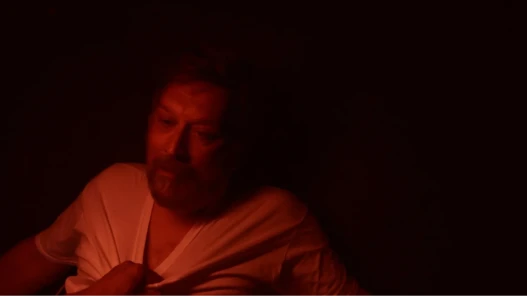 A man in a dark room illuminated by red light that is being held on the ground by another person