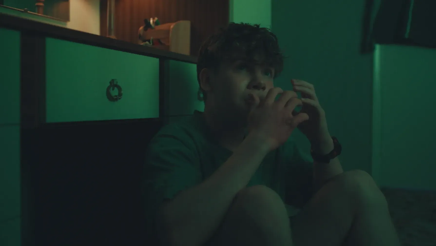 A teenage boy seated in a room bathed in green light
