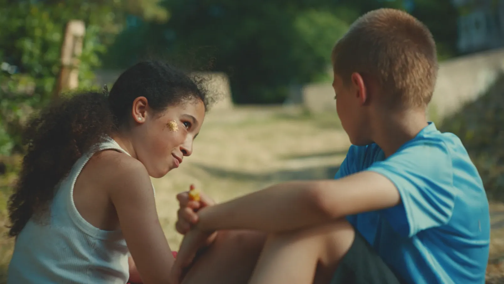 Two children seated outside eating chips