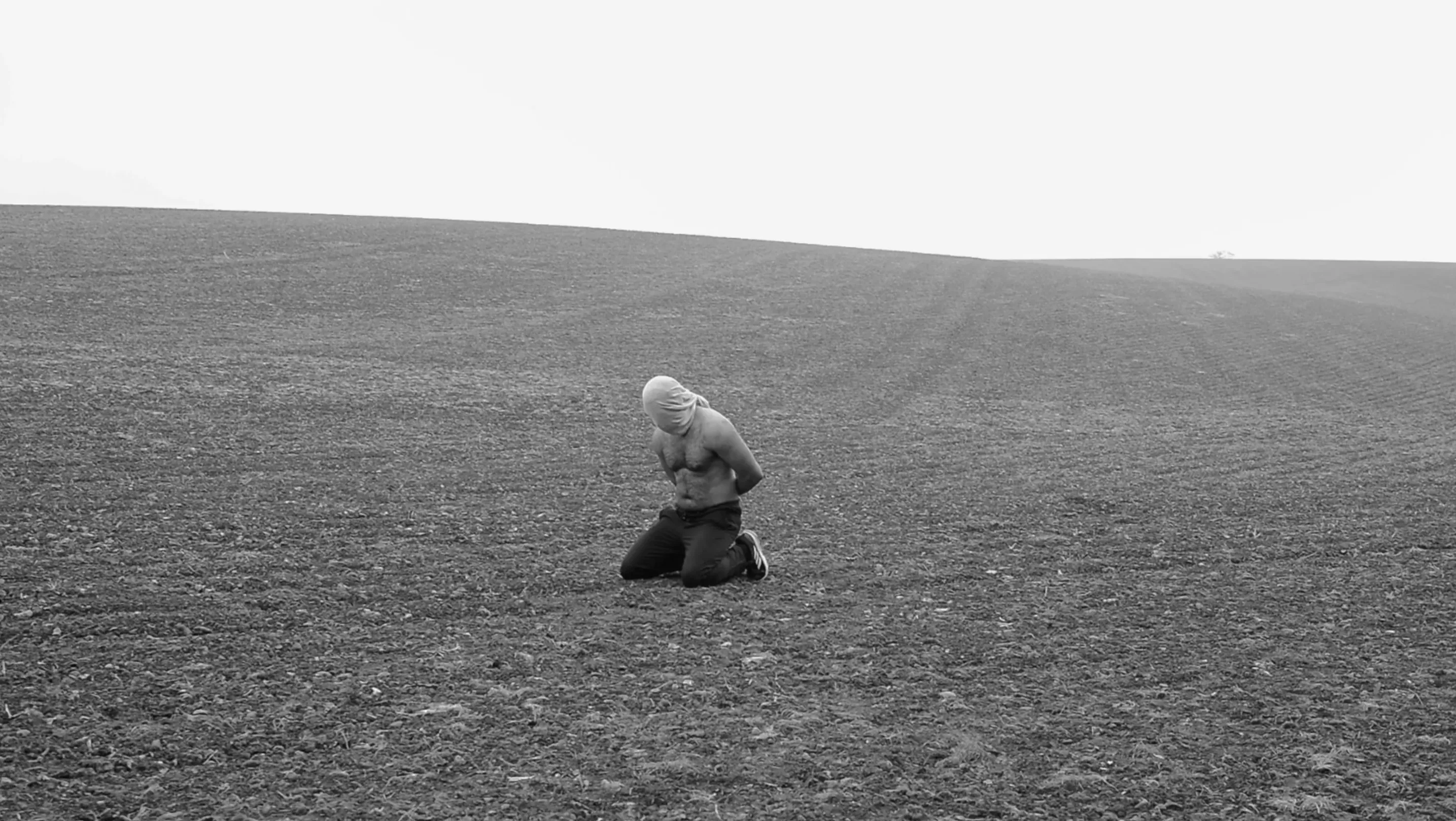 A man with a hood over his head kneeling in an outside space waiting to be executed