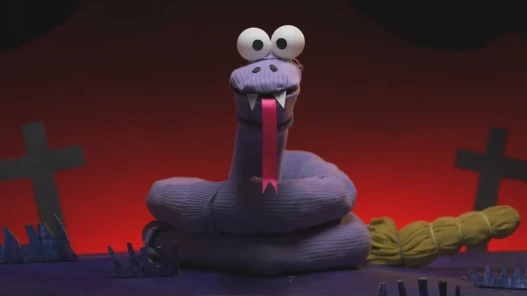 A sock puppet snake stares into the camera in a cardboard graveyard.