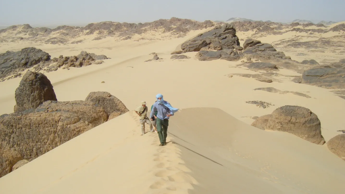Men walk along a sand dune in the Sahara.