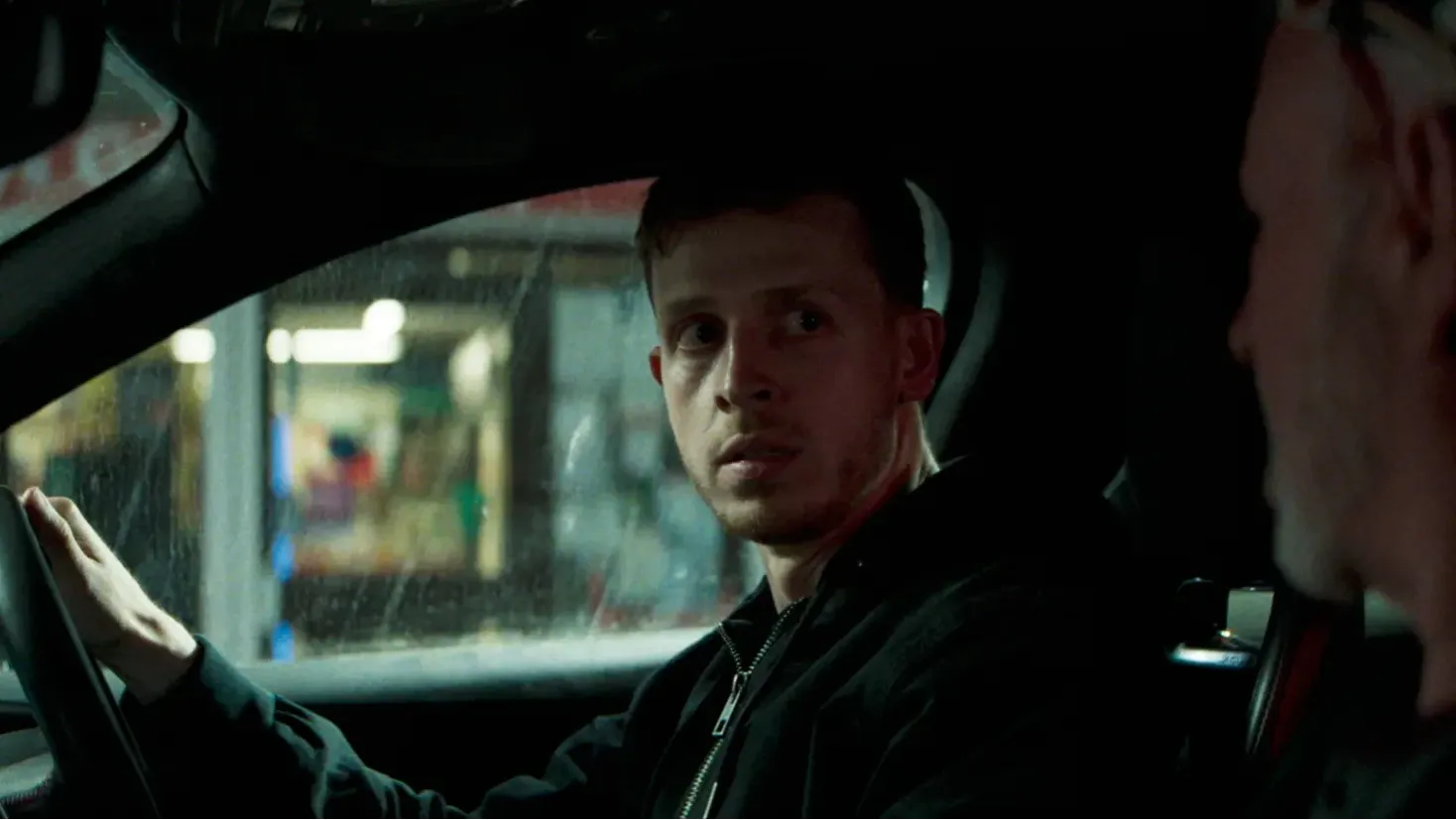 Two men in the front seats of a car, looking at each other 