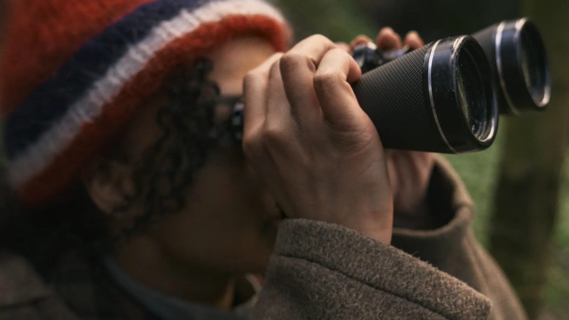 A mixed race woman in a red hat uses binoculars
