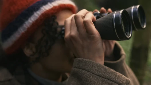 A mixed race woman in a red hat uses binoculars