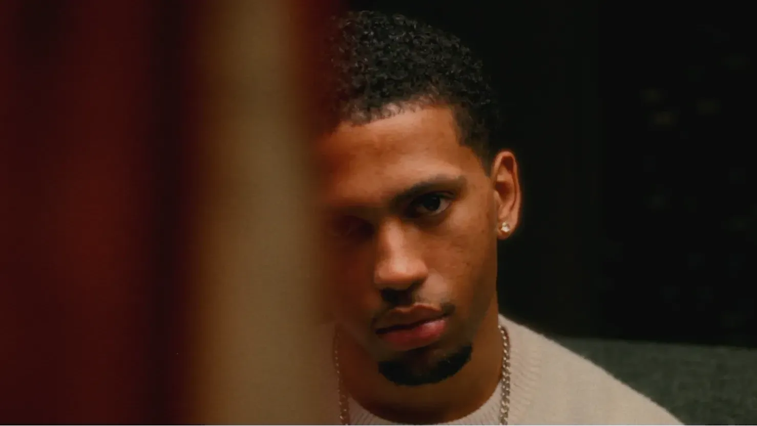 A young man stares forward, surrounded by darkness, with some passing by distorting one side of his face