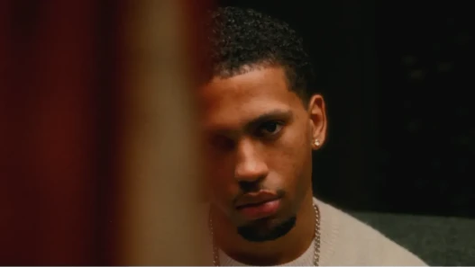 A young man stares forward, surrounded by darkness, with some passing by distorting one side of his face
