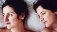 Close up double portrait of two women next to one another in bed smiling