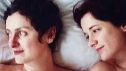 Close up double portrait of two women next to one another in bed smiling