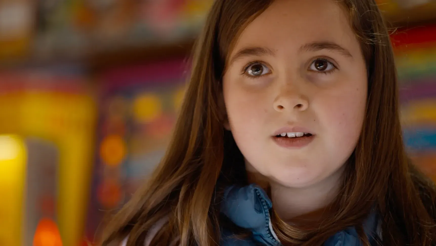 A young girl with the lights of an amusement arcade behind her