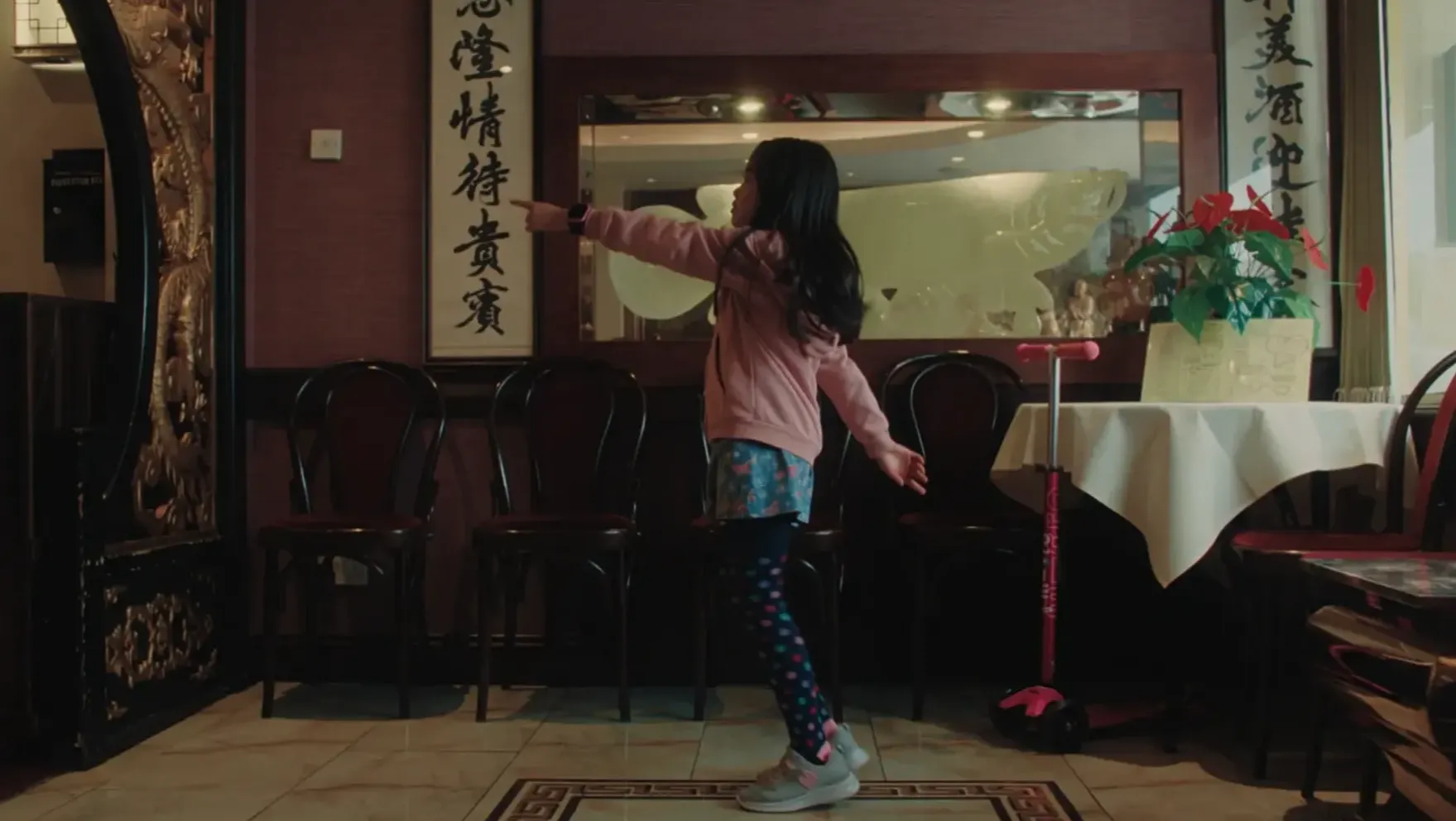 A young girl, pointing at something inside a Chinese restaurant lobby.