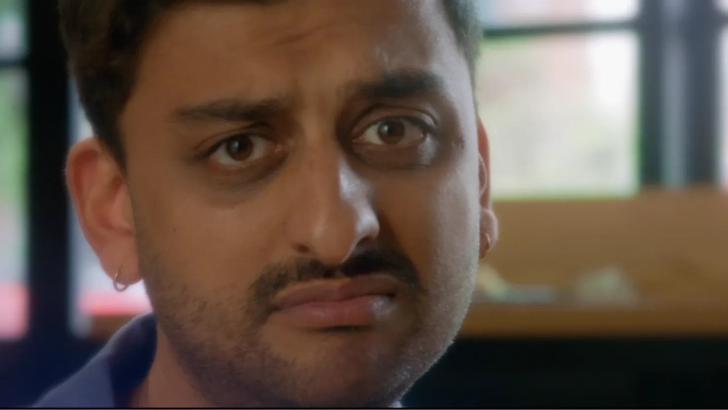 A close up of a young man with a goatee and earrings, looking sad and wistful