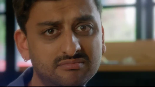 A close up of a young man with a goatee and earrings, looking sad and wistful