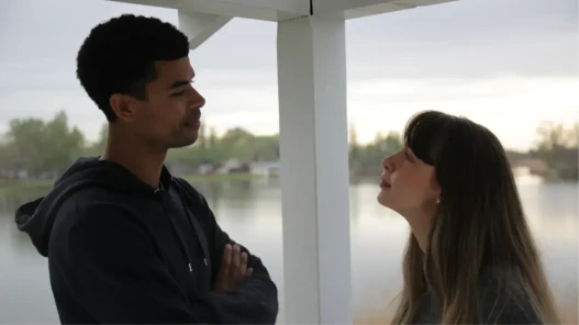 A man and a woman standing outside with a view of a lake behind them.