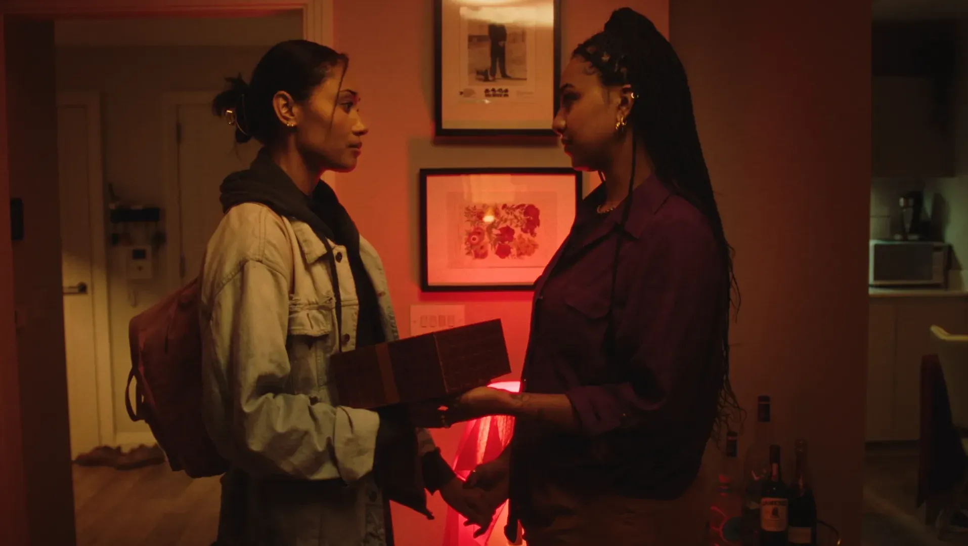Two women hold each other's gaze and hands with a gift box between them.