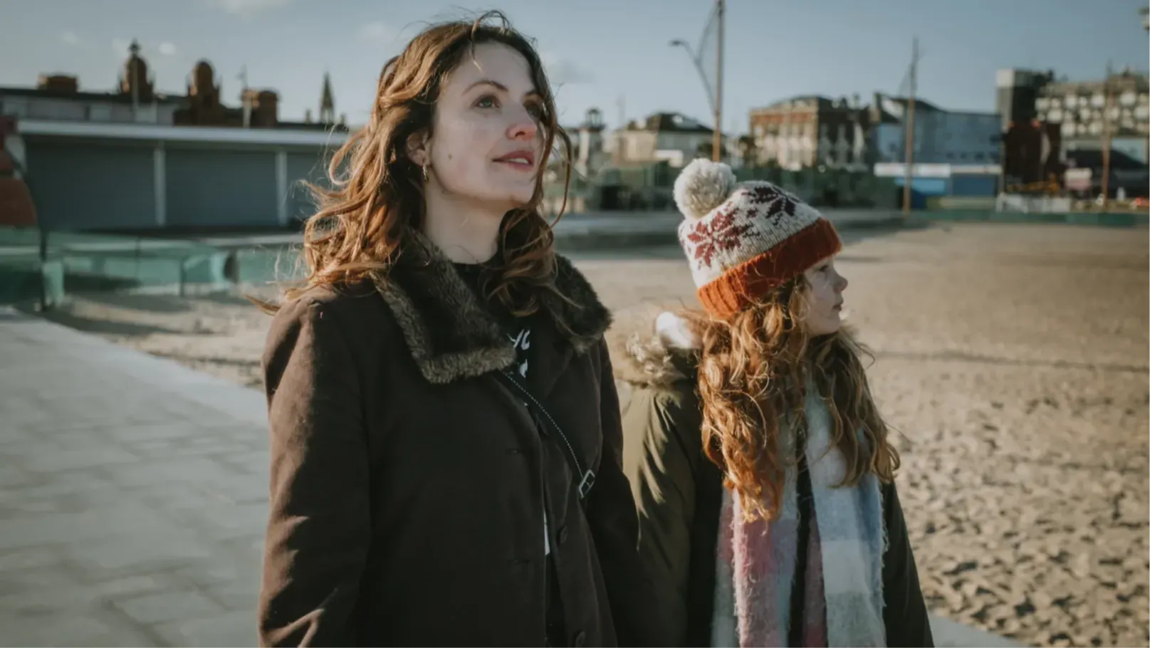 A woman and a girl walk at the side of a beach.