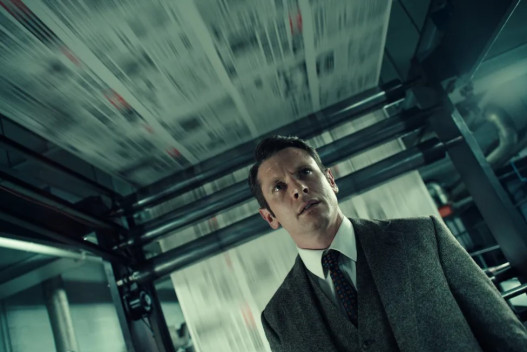 A man in a suit stands in front of a newspaper printing press