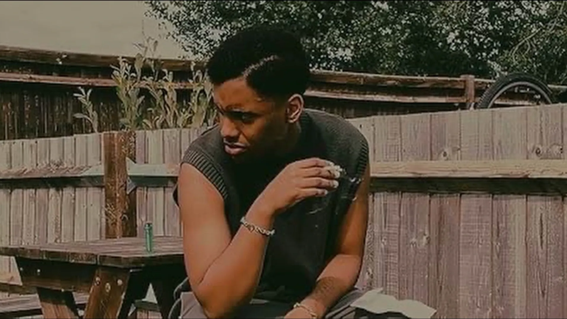 A man sits on a wooden bench smoking a cigarette