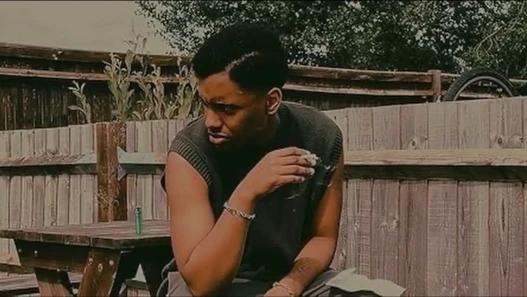 A man sits on a wooden bench smoking a cigarette