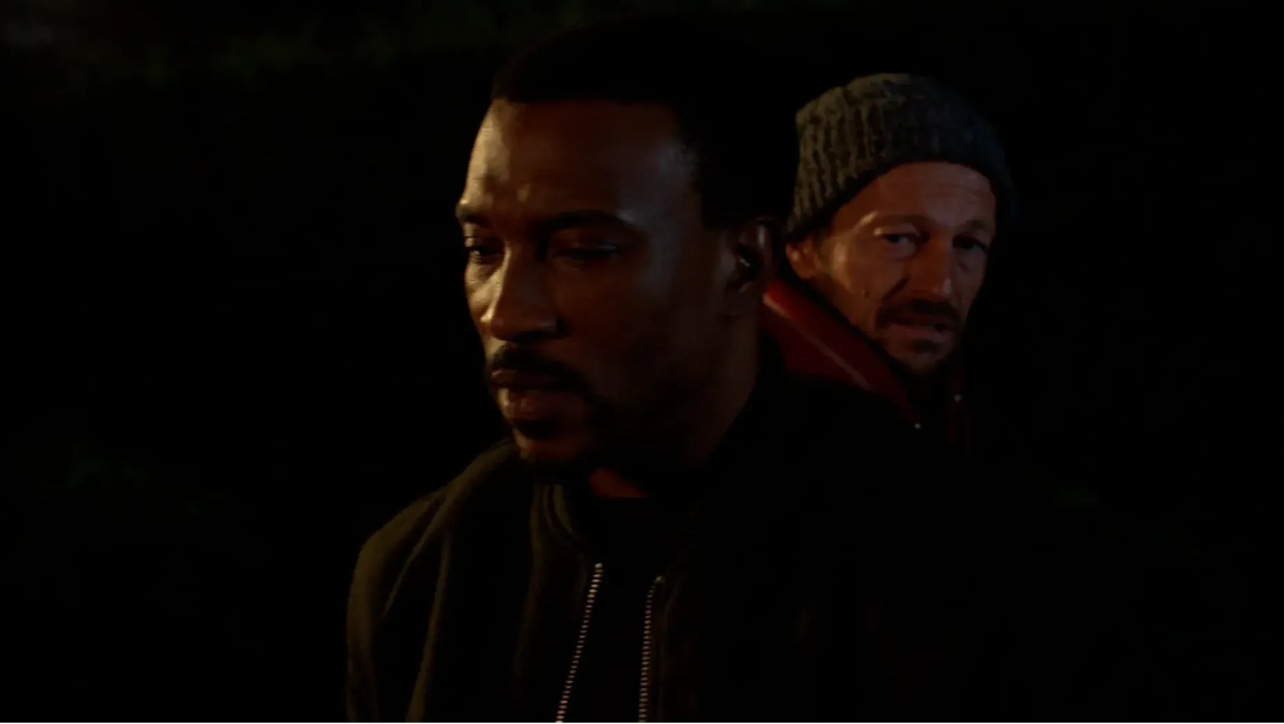 Two men's faces in shadows with low light and a black background