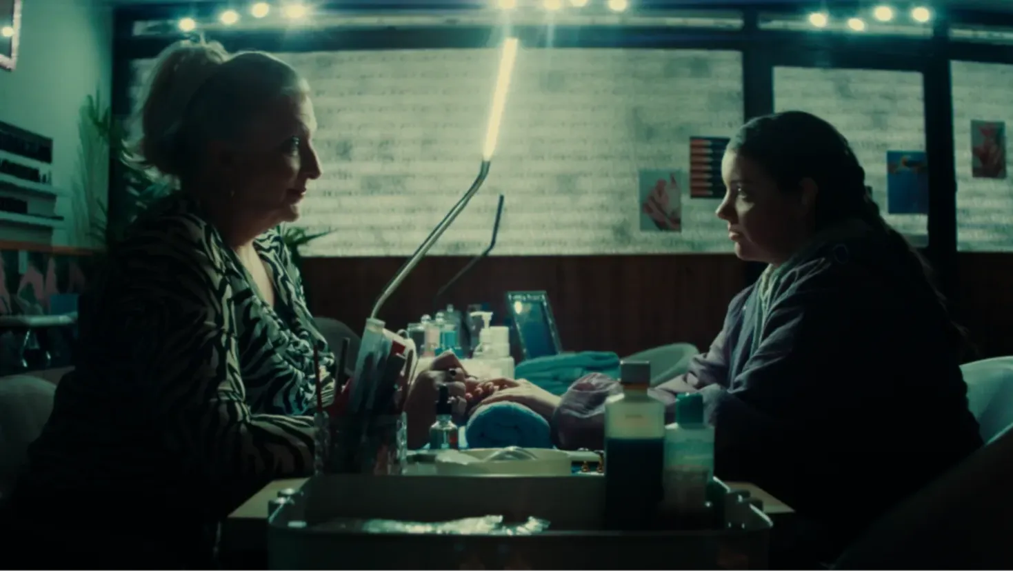 An older woman and a young teenager sit opposite eachother in a nail salon.