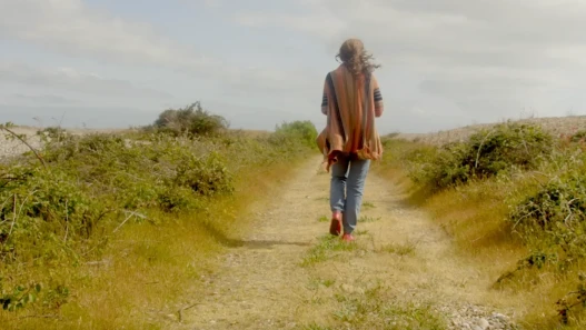 A woman walking down a path towards an open horizon with the sky above