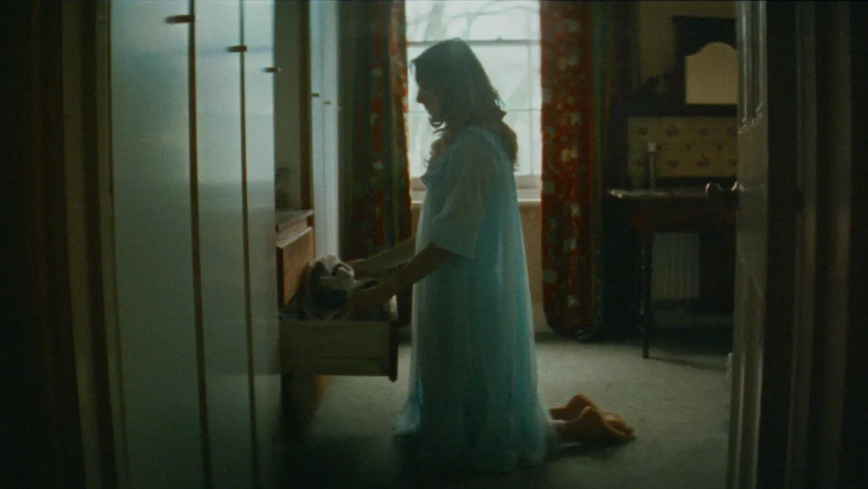 A woman in a nightdress kneeling at a drawer
