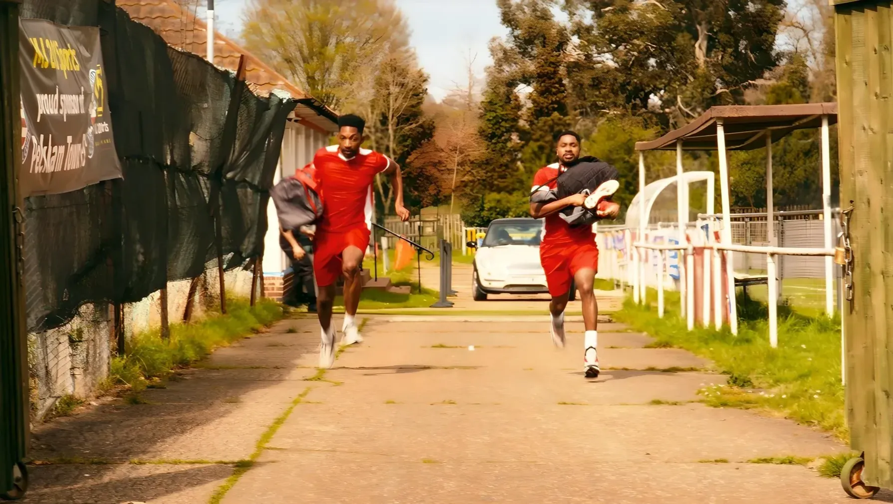 Two young Black men running together outside a football ground.
