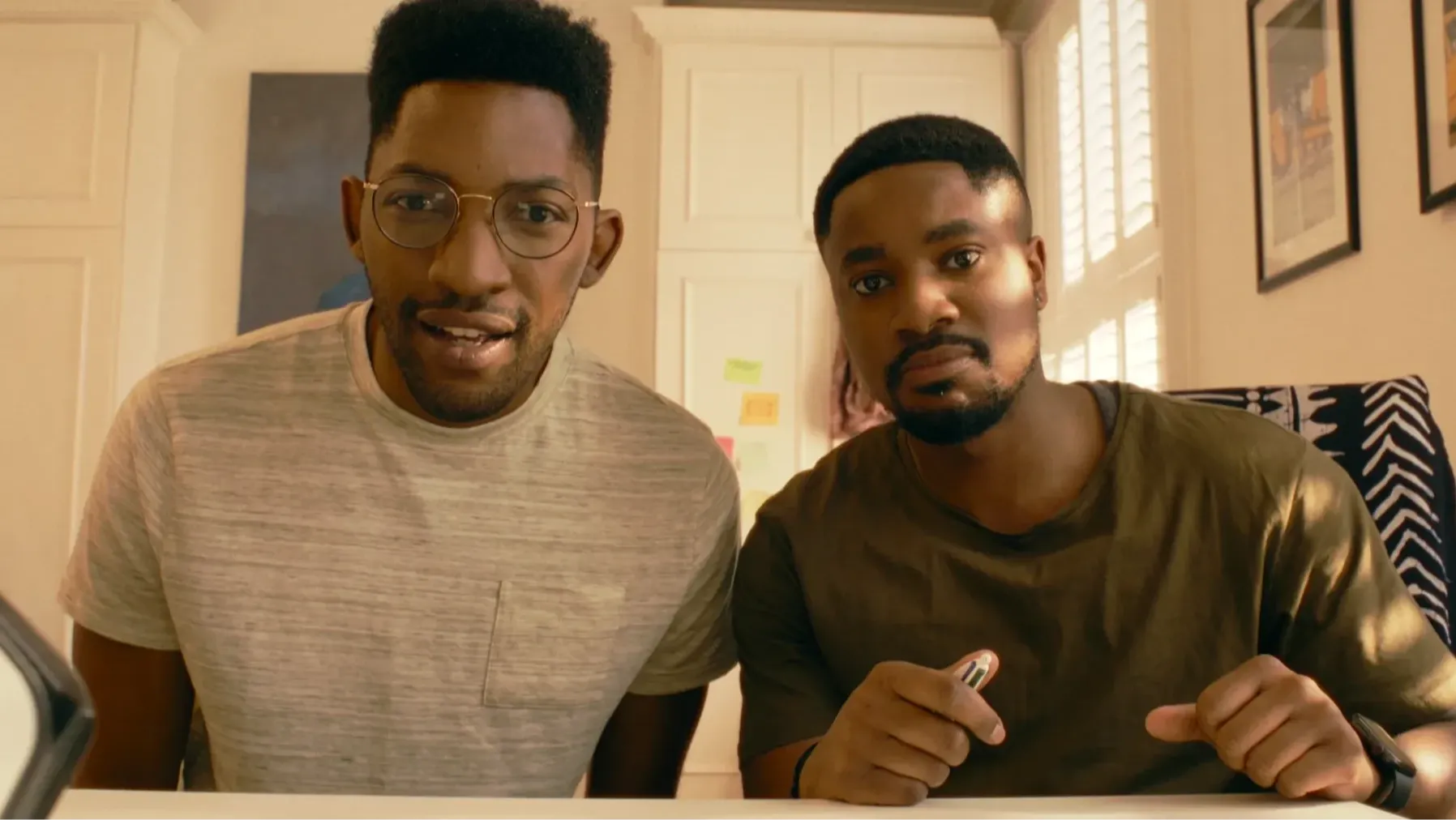 Two young Black men sitting side by side indoors, looking towards the screen with shocked expressions.