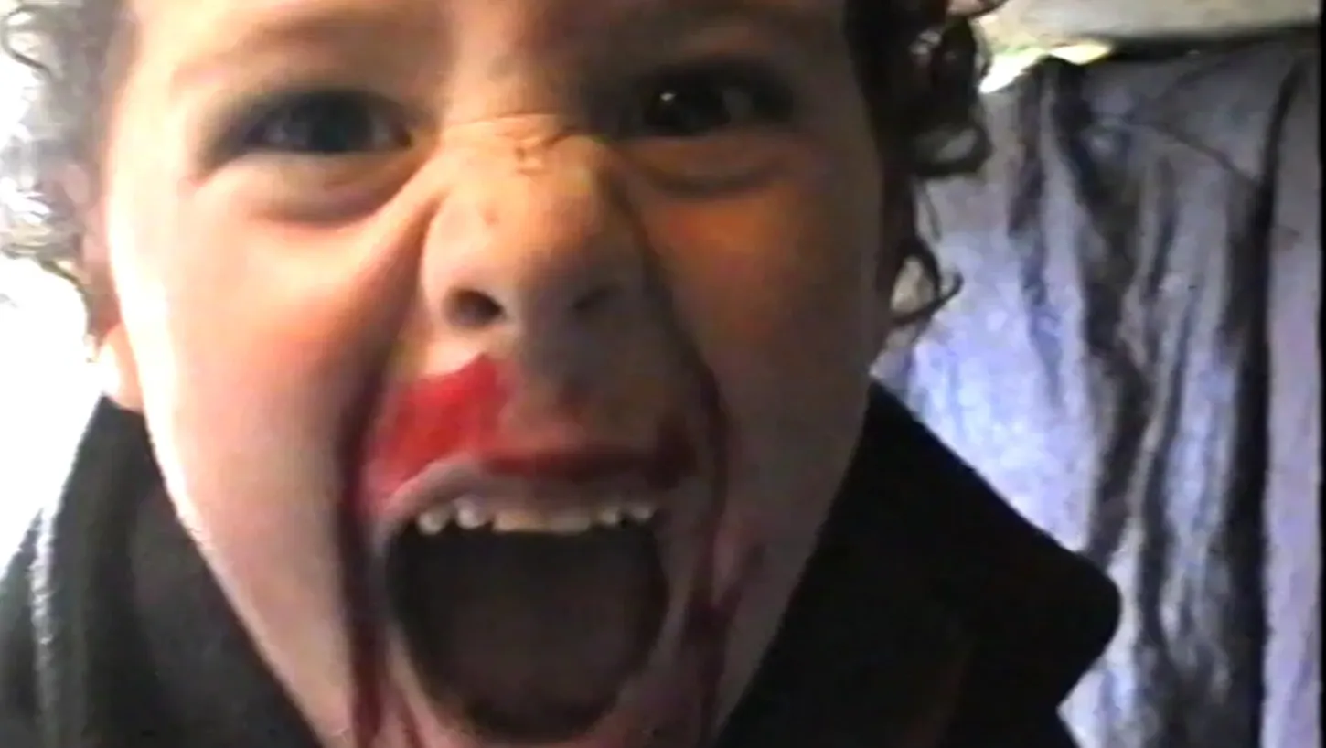 Patrick Hough as a child:  Close-up of Patrick Hough as a child, looking directly into the camera with his mouth open and red pigment smeared across his face.
