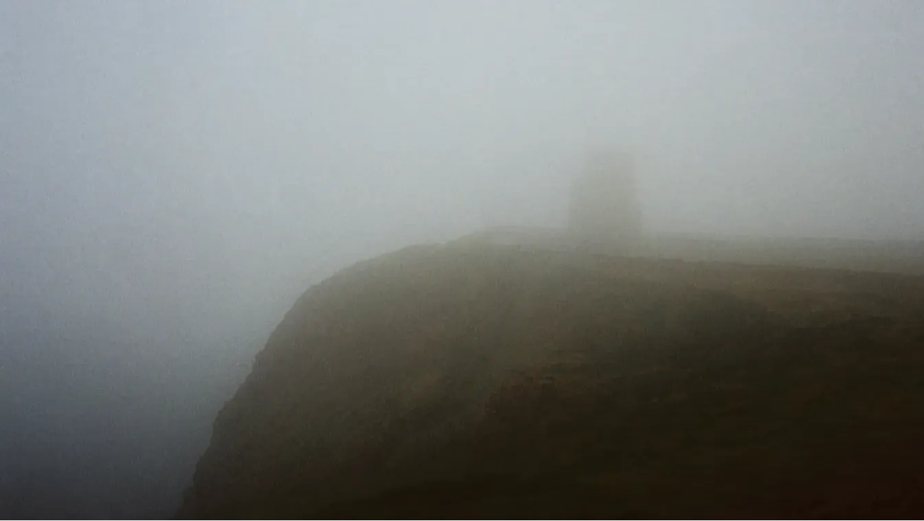 Cliff edge shrouded in fog, with the outline of a small building.