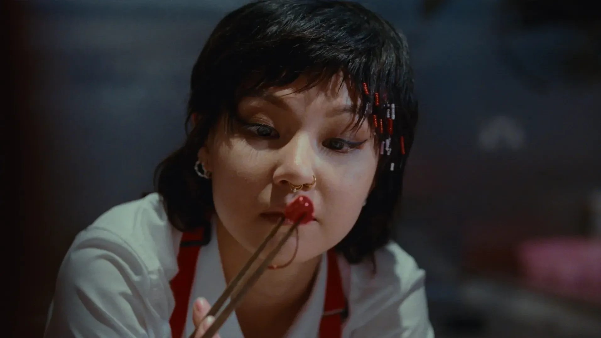 A woman eyes a cherry pinched between chopsticks