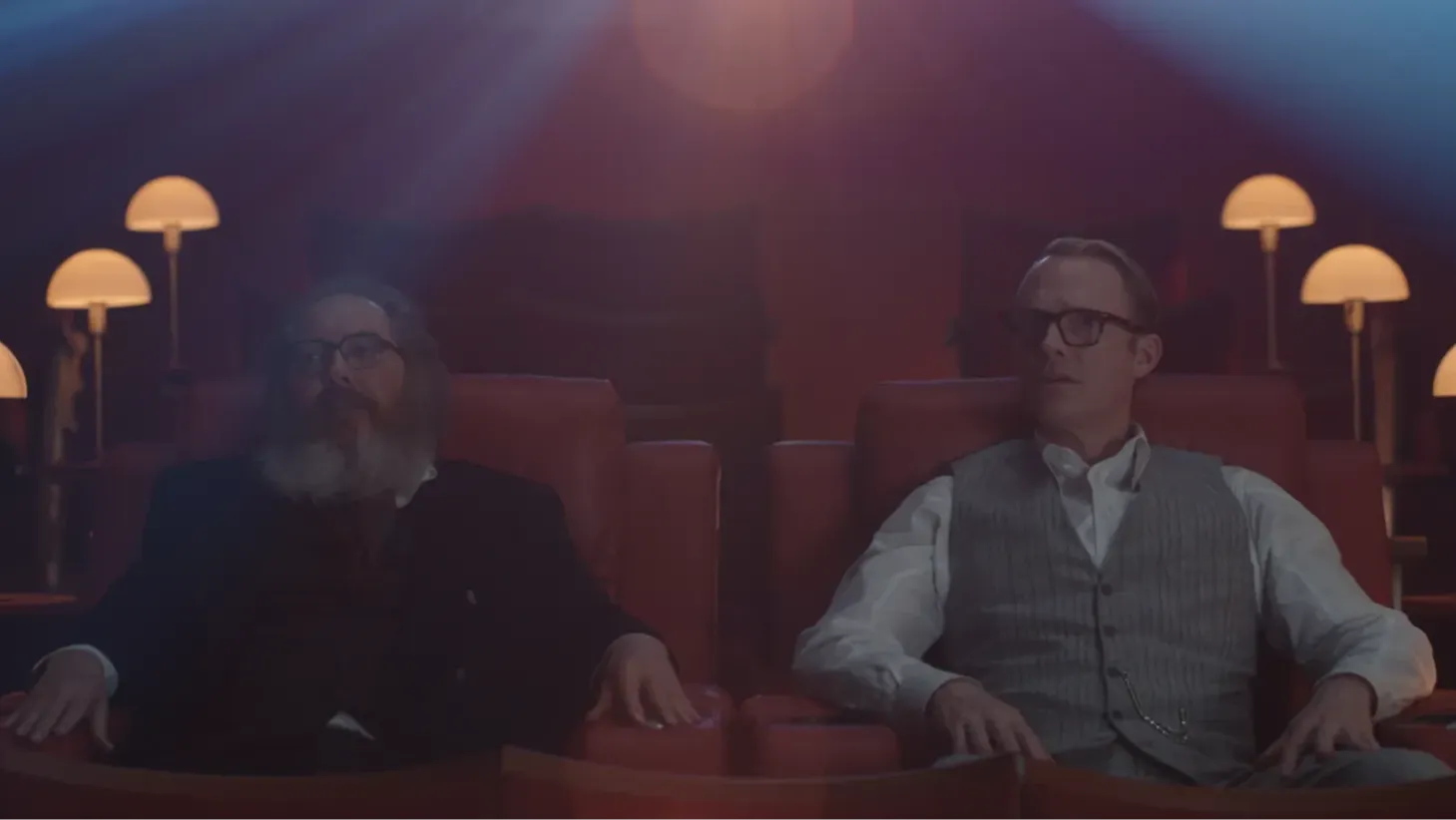 Two men sit side by side in a cinema facing forward