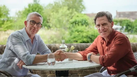 Two men shaking hands over table and smiling to camera.
