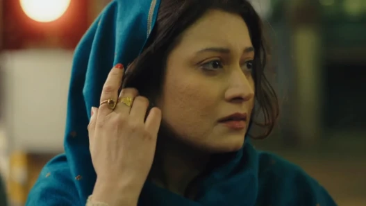 Woman in blue headscarf looks to the side with one hand holding her scarf away from her face 