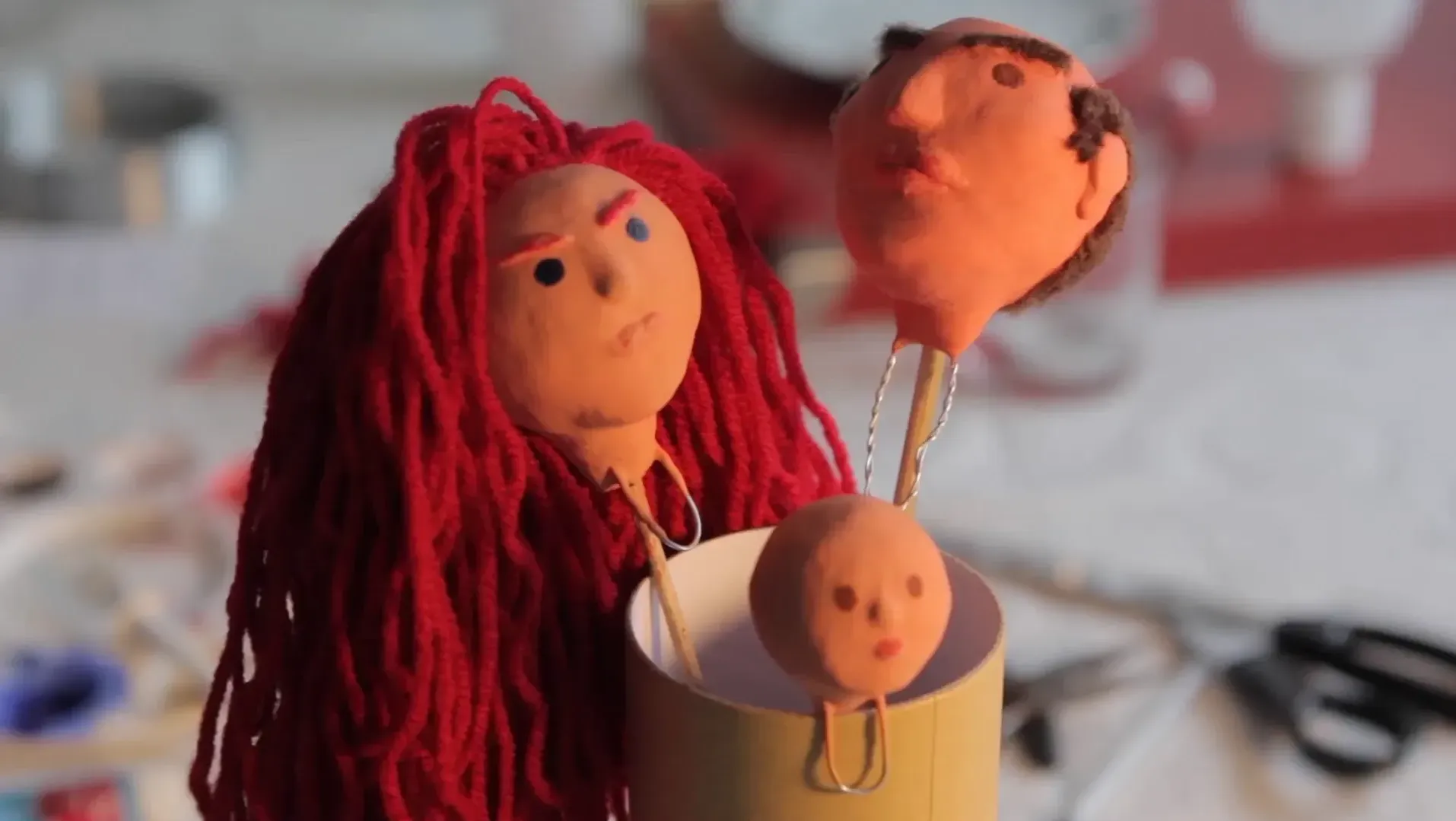 3 puppet heads on sticks with a blurred background of scissors, paint palette