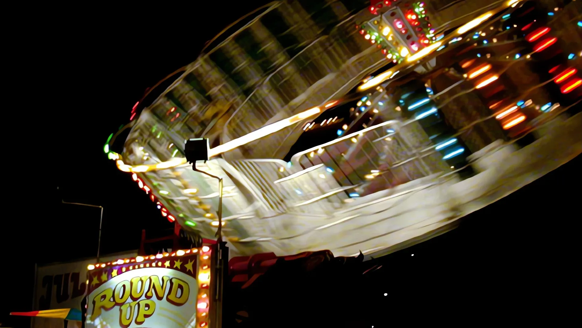 A spinning fairground ride lit at night, blurred with motion