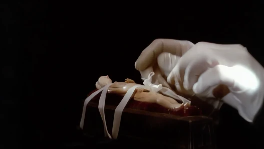 Gloved hands untying a small wrapped parcel on a dark table