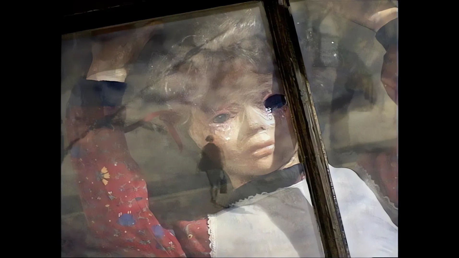 A puppet girl in a red flowered dress presses against a window, a walking figure reflected in the glass