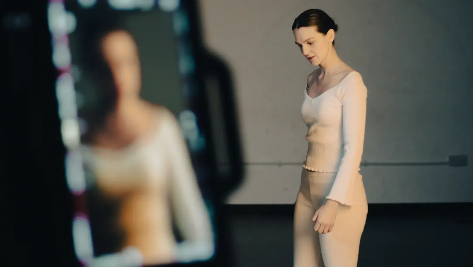 A white woman dressed in white activewear walks deep in thought in the background. Out of focus in the foreground is the playback screen of a camera with her on it.
